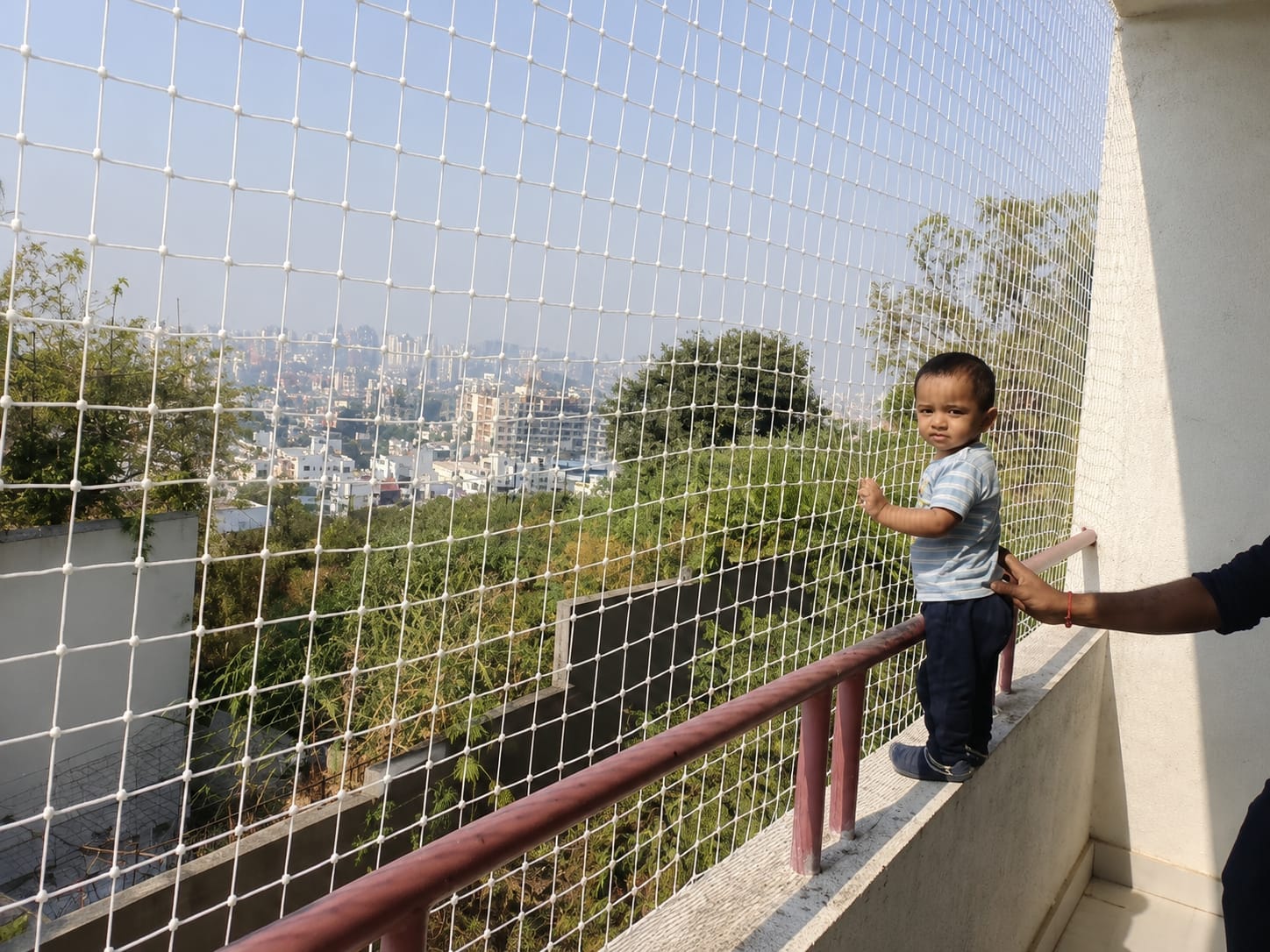 Child standing safely at a balcony protected by a children safety net
